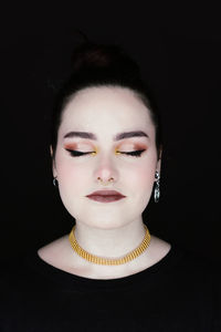 Close-up portrait of a serious young woman over black background