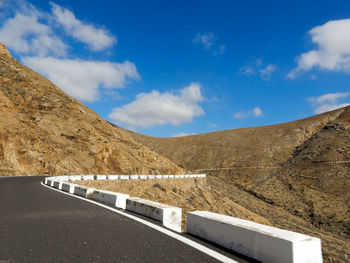 Road leading towards mountains against blue sky