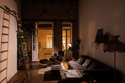 Interior of living room with green potted plants and comfortable sofa in flat in loft style at night