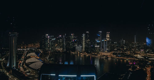 Illuminated buildings by river against sky at night