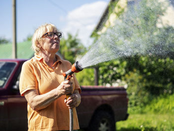 Smiling woman watering plants while holding garden hose