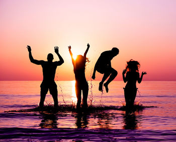 Silhouette friends in sea against sky during sunset