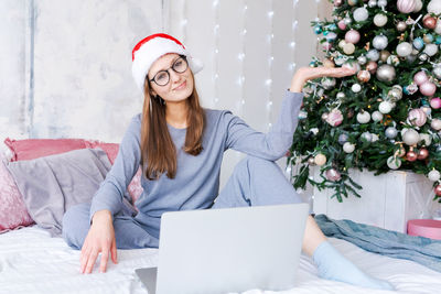 Young woman in santa hat gesticulates with her hands while chatting via video