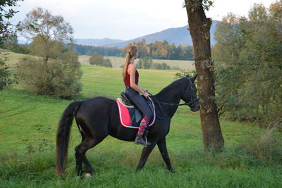 Full length of young woman horseback riding on grassy field
