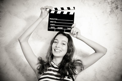 Portrait of smiling young woman holding film slate against wall