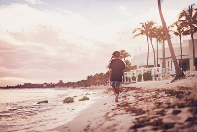 Rear view of man standing at beach against sky