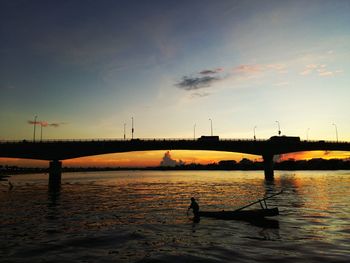 Silhouette man in boat against sky during sunset