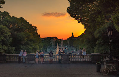 Group of people by plants against sky during sunset