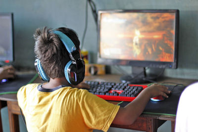 Rear view of boy playing on computer
