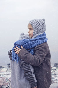 Cute smiling siblings embracing by lake during winter