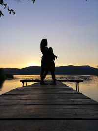 Woman on pier over lake against sky during sunset