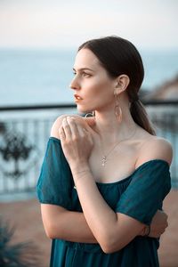 Young woman looking away while standing by sea