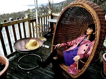 Young woman sitting in rattan chair on porch