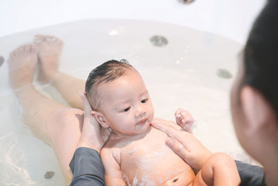 Low section of mother bathing baby daughter in bathtub