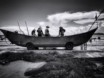 People on boat at beach against sky