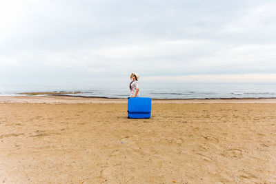 Woman standing behind suitcase at beach
