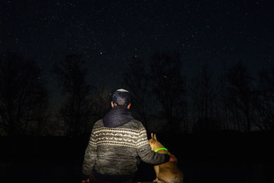 Rear view of man with dog in forest against star field at night