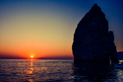 Silhouette rock formation in sea against clear sky during sunset