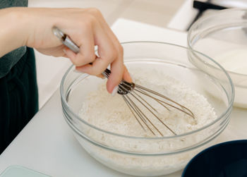 The hand of a caucasian young girl mixes the dough with a whisk in a bowl.