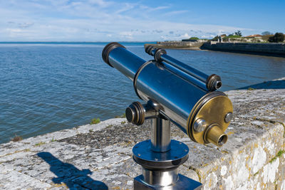 Coin-operated binocular by sea against sky