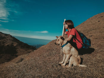 Woman with dog sitting on mountain against sky