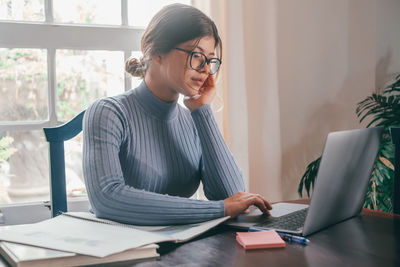 Side view of young woman using laptop at home