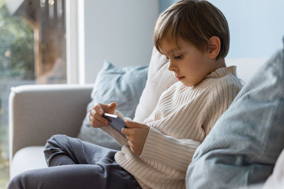 Side view of a little boy in the living room using a digital tablet.