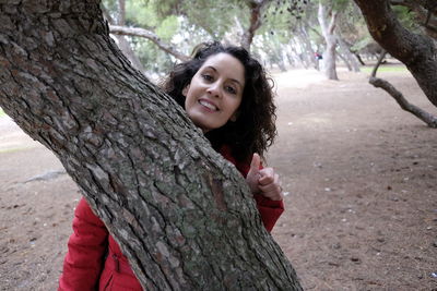 Portrait of smiling young woman against tree trunk