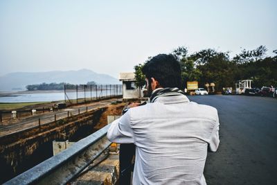 Rear view of man standing by railing against sky