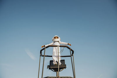 Boy wearing space suit standing with arms outstretched on chair