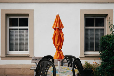 Closed orange parasol in front of wall with windows