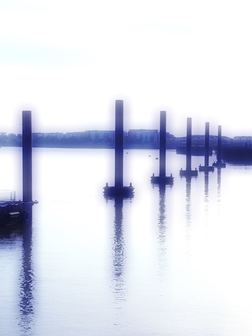 REFLECTION OF WOODEN POSTS IN RIVER AGAINST SKY