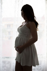 Side view of a young woman standing against window