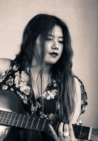 Young woman playing guitar while sitting against wall