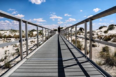 Man standing on footbridge against sky