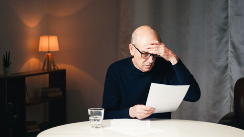 Elderly man sitting at the table reads his electricity and gas bills