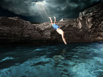 Man diving in sea by rock formation against sky