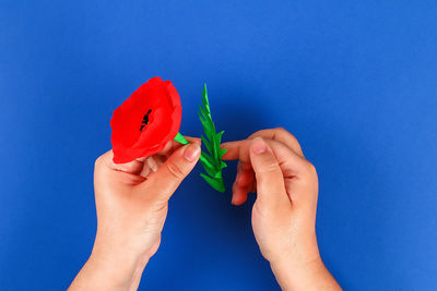 Close-up of hand holding red leaf against blue wall