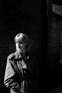 Young woman looking away against brick wall