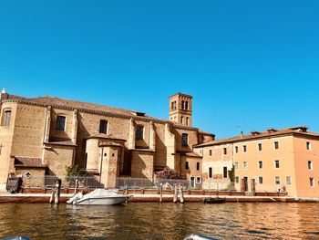 Buildings in canal against clear blue sky