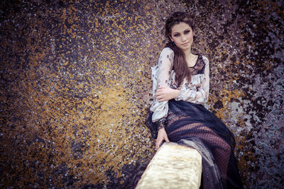 Portrait of young woman sitting against wall