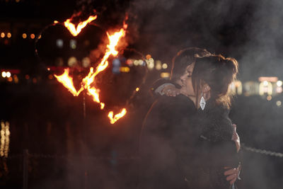 Side view of couple embracing while standing against sky at night