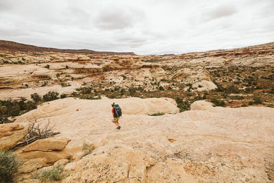 Female backpacker walks down a sandstone rock face in utah desert