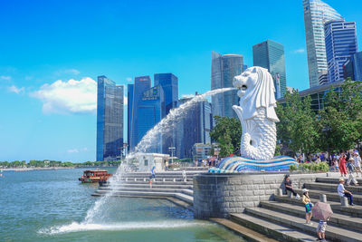 Statue by fountain in city against sky