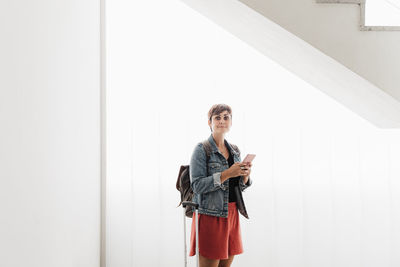 Young woman using phone while standing on laptop