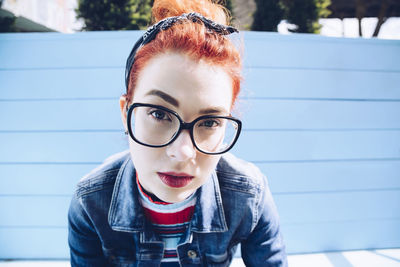 Portrait of redhead young woman wearing eyeglasses while sitting on bench