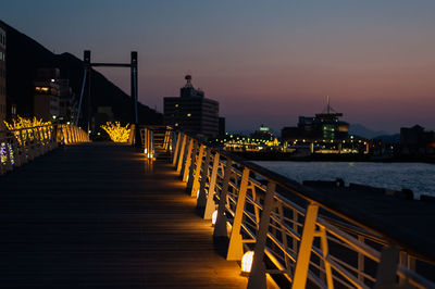 Illuminated bridge over sea against sky at night