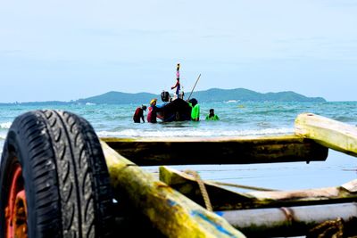 Close-up of trolley with people holding boat in sea against sky