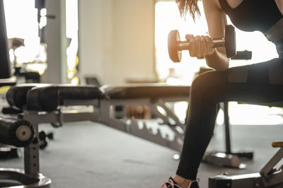 Midsection of woman lifting dumbbell in gym