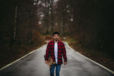 Portrait of young man standing on road in forest